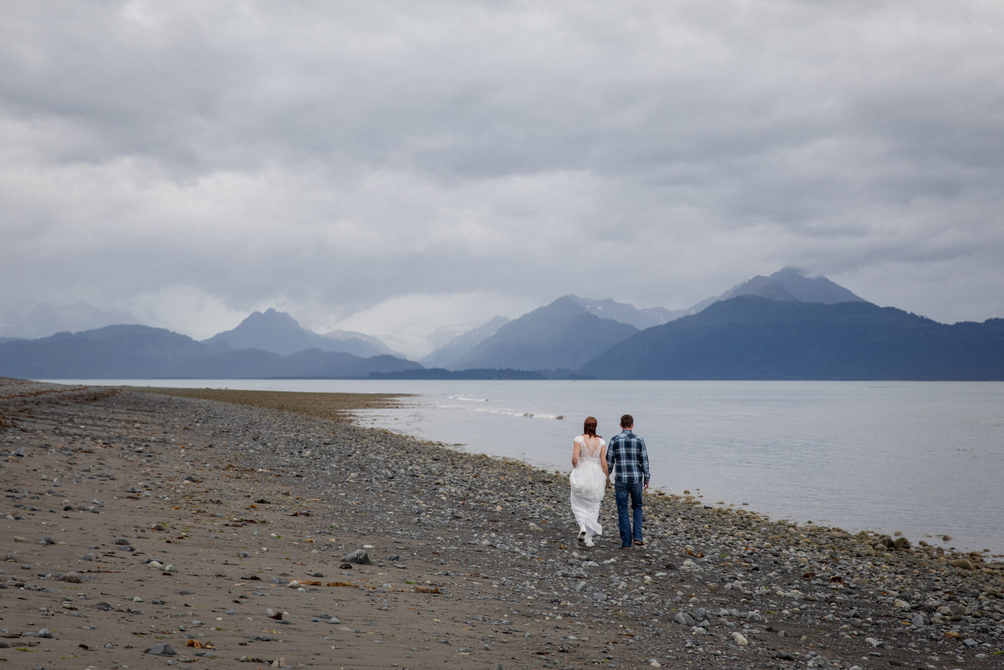couple walking along a quiet Bishop's Beach while eloping in Homer with expansive coastline and layered mountains in the distance