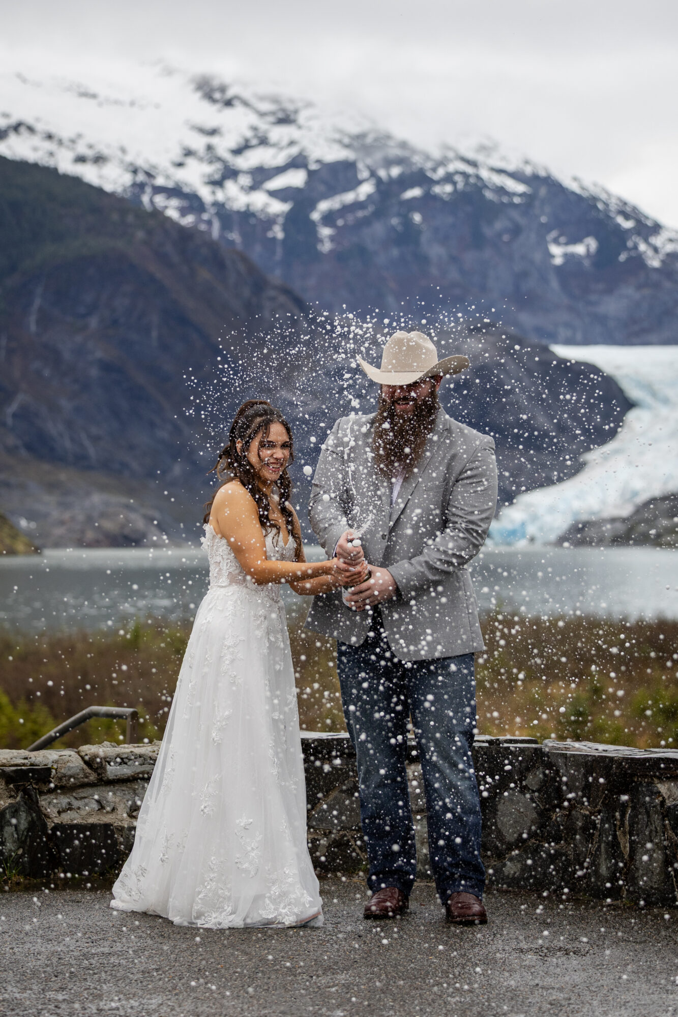 Couple celebrating with champagne in front of Mendenhall Glacier near Juneau, Alaska during an elopement.
