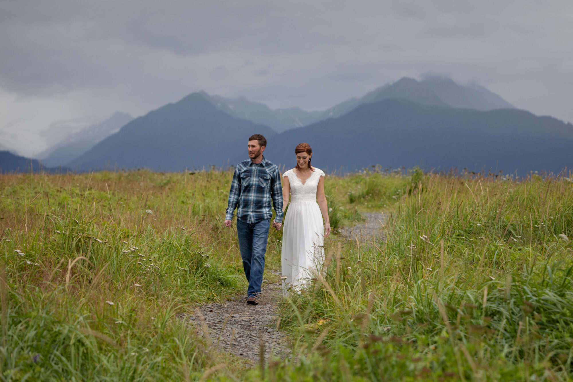 couple walking hand in hand on a coastal trail during their Homer, Alaska elopement with mountains rising in the background