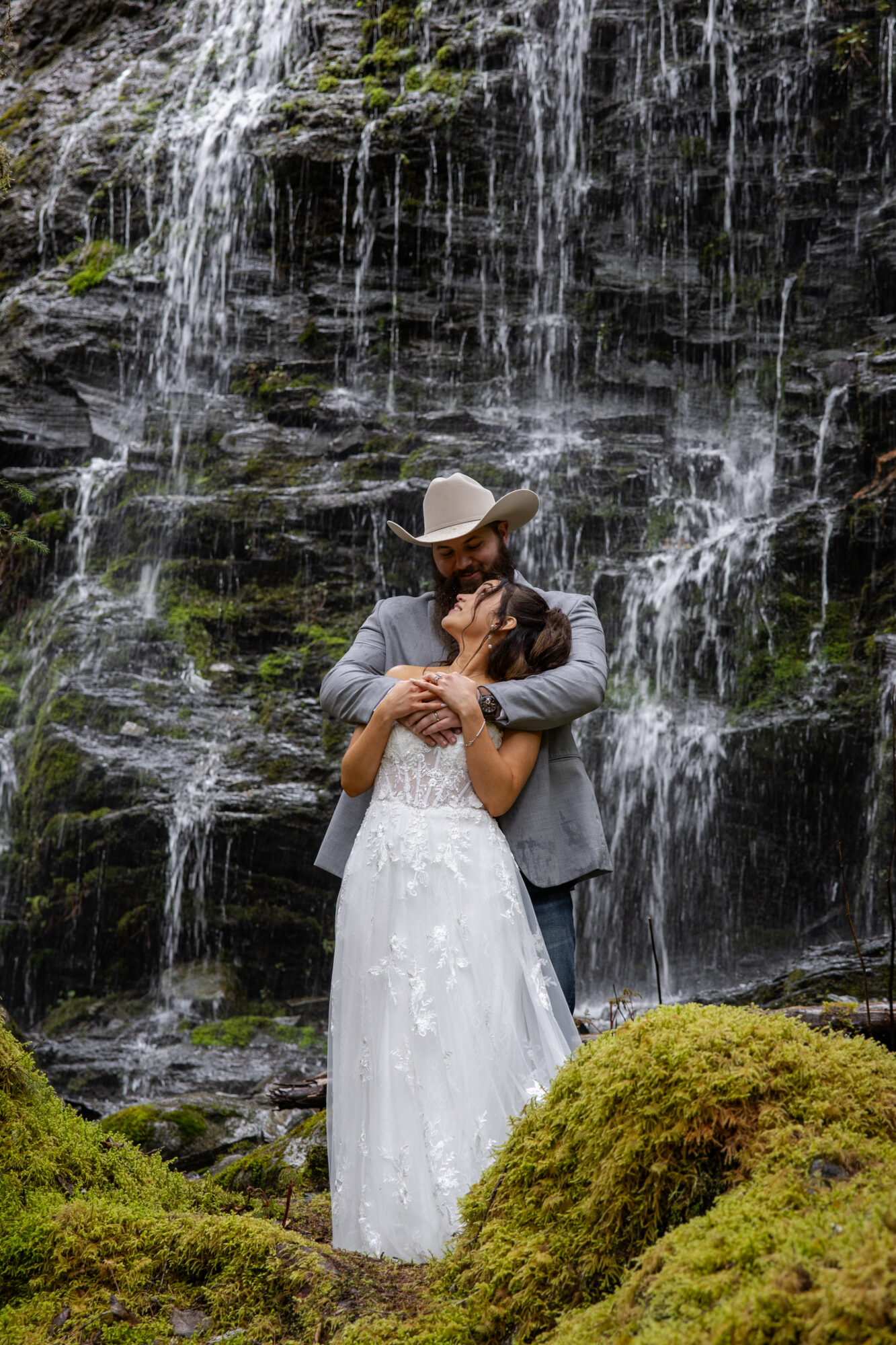 Couple embracing in front of a waterfall near Juneau, Alaska during an intimate forest elopement.