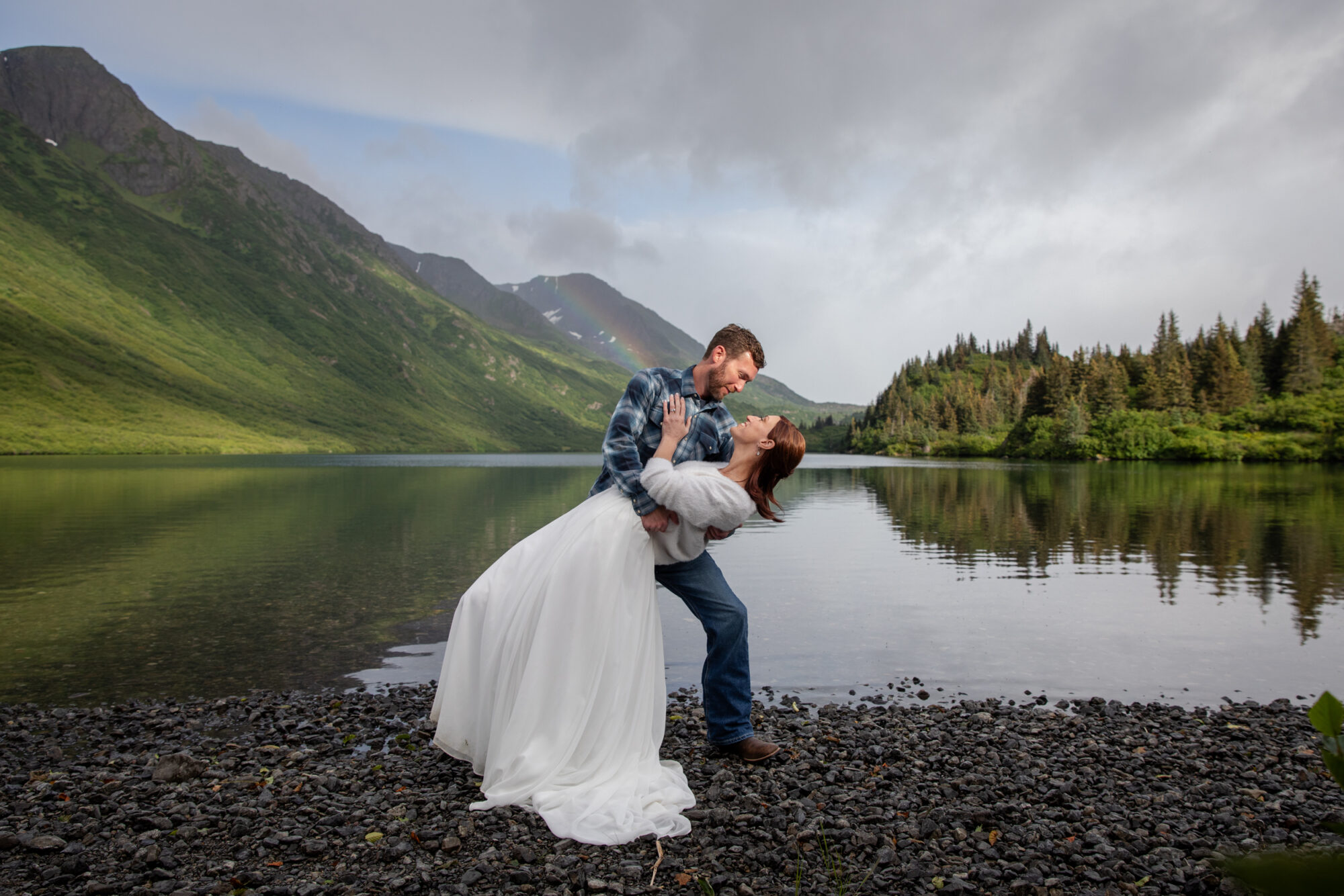 couple celebrating their elopement in Homer, Alaska with a lakeside kiss and mountains reflecting in the water