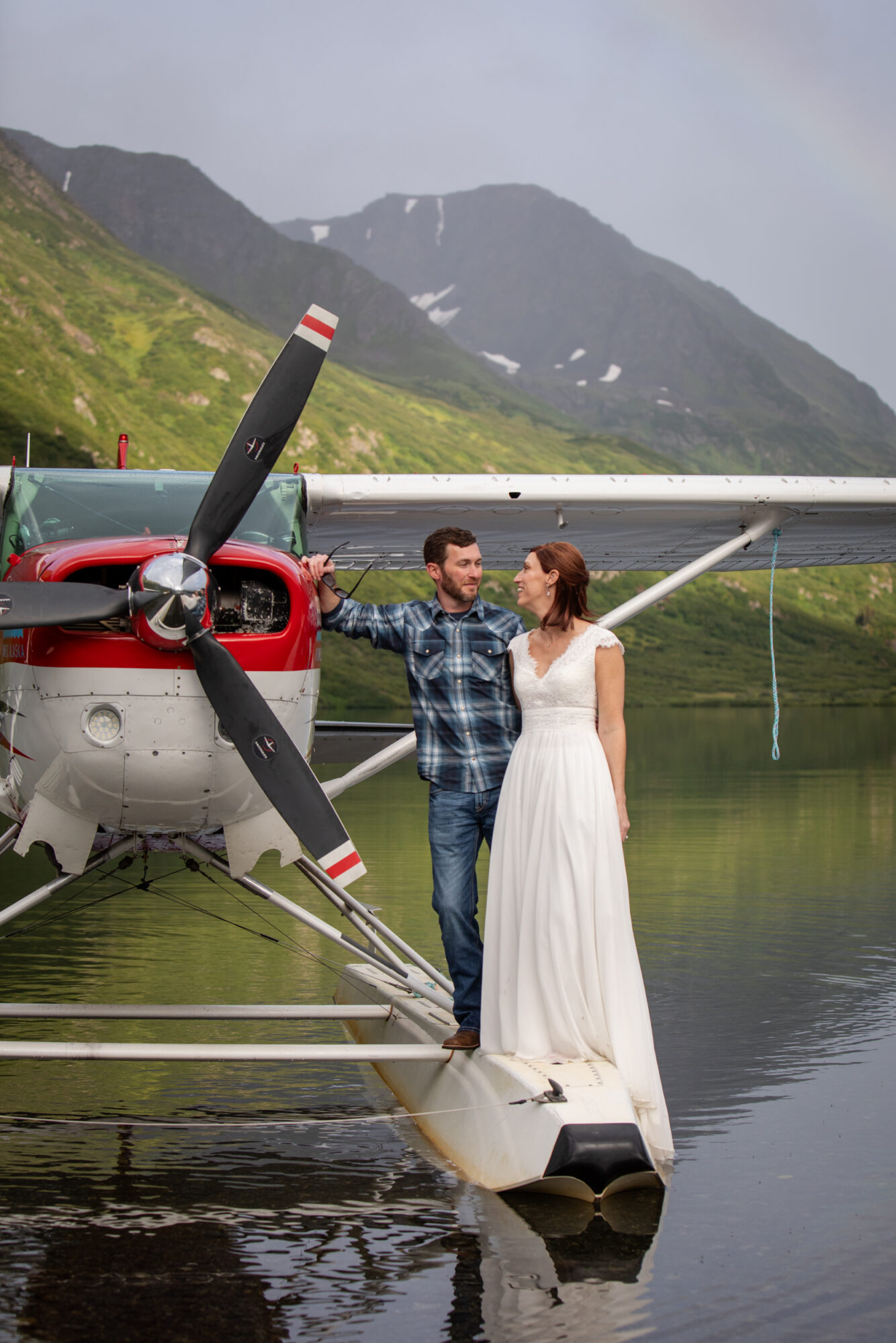 couple standing on a floatplane during their Homer Alaska elopement with mountains and calm lake in the background
