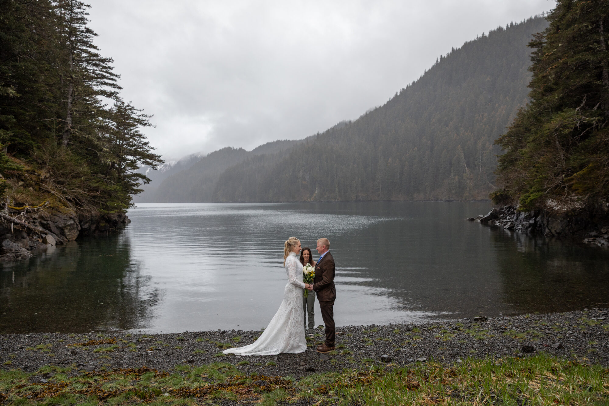 couple exchanging vows during their Homer, Alaska elopement beside a secluded Kachemak Bay cove surrounded by forest and mountains