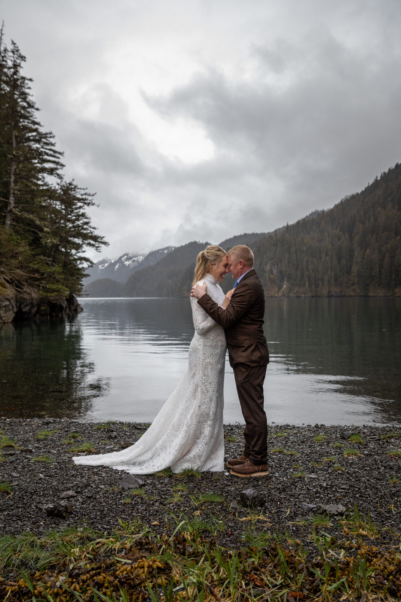 couple sharing a quiet moment during their Homer, Alaska elopement beside a calm bay with foggy mountains in the background