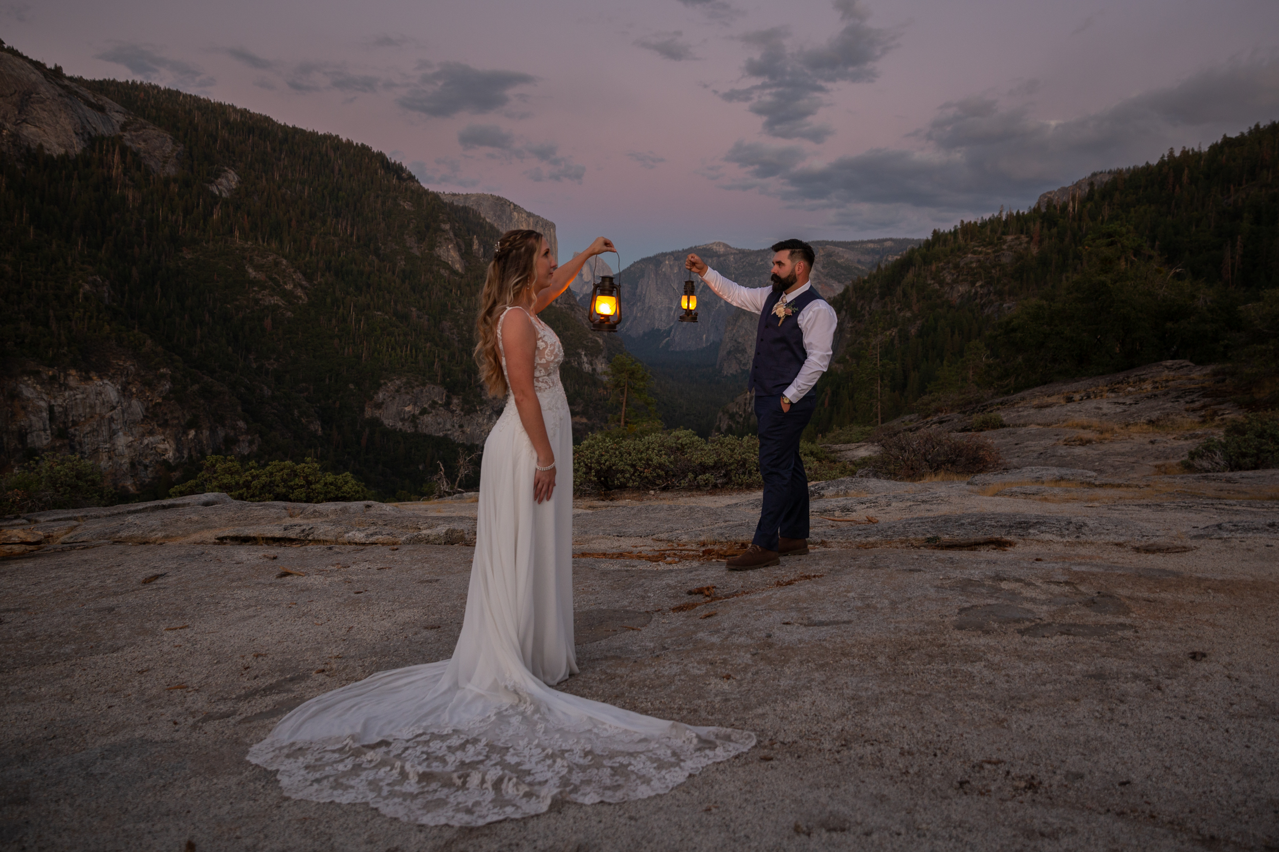 Bride & Groom hold lanterns in the fading light with Yosemite Valley and pink skies in the background.