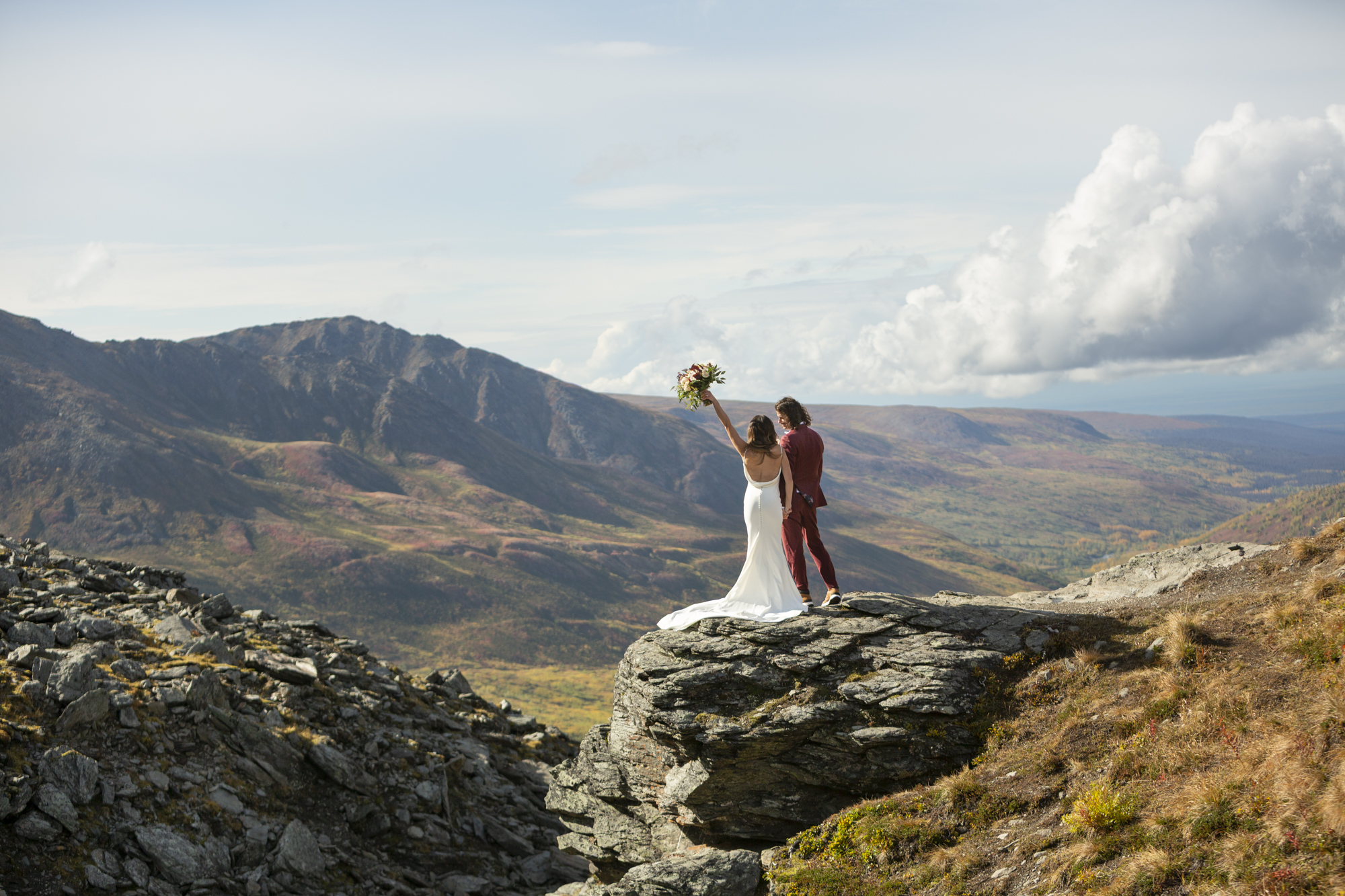 Couple standing on a rocky mountain overlook with sweeping valley views during an adventurous Alaska elopement.