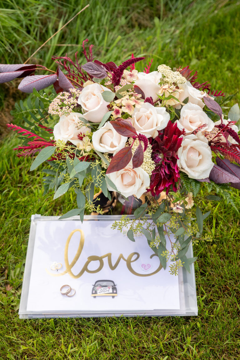 A red and white floral bouquet is in a green grassy field with a card that says love on it.