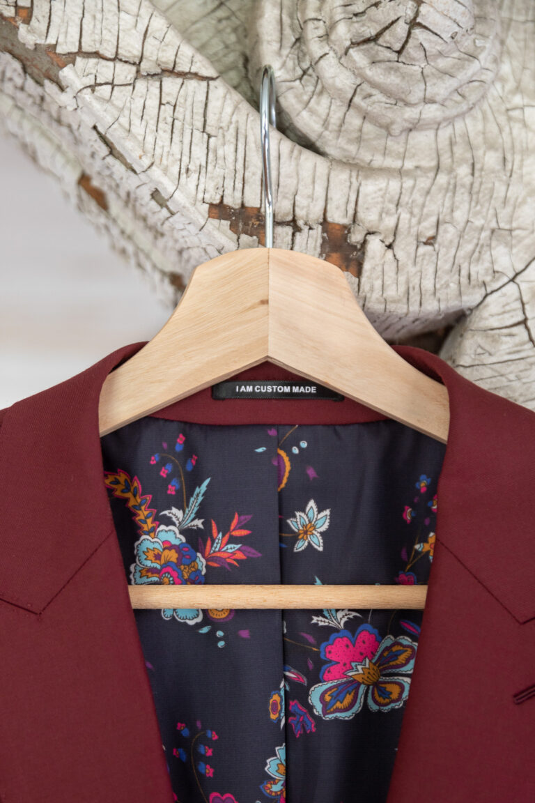 A maroon suit with flowers on the inside hangs from a hanger.