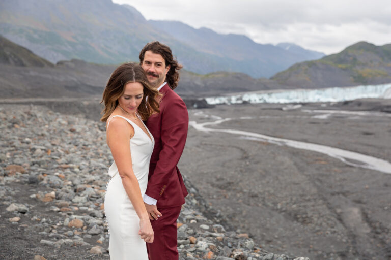 A bride and groom stand next to each other in front of a glacier in Alaska on their elopement day.