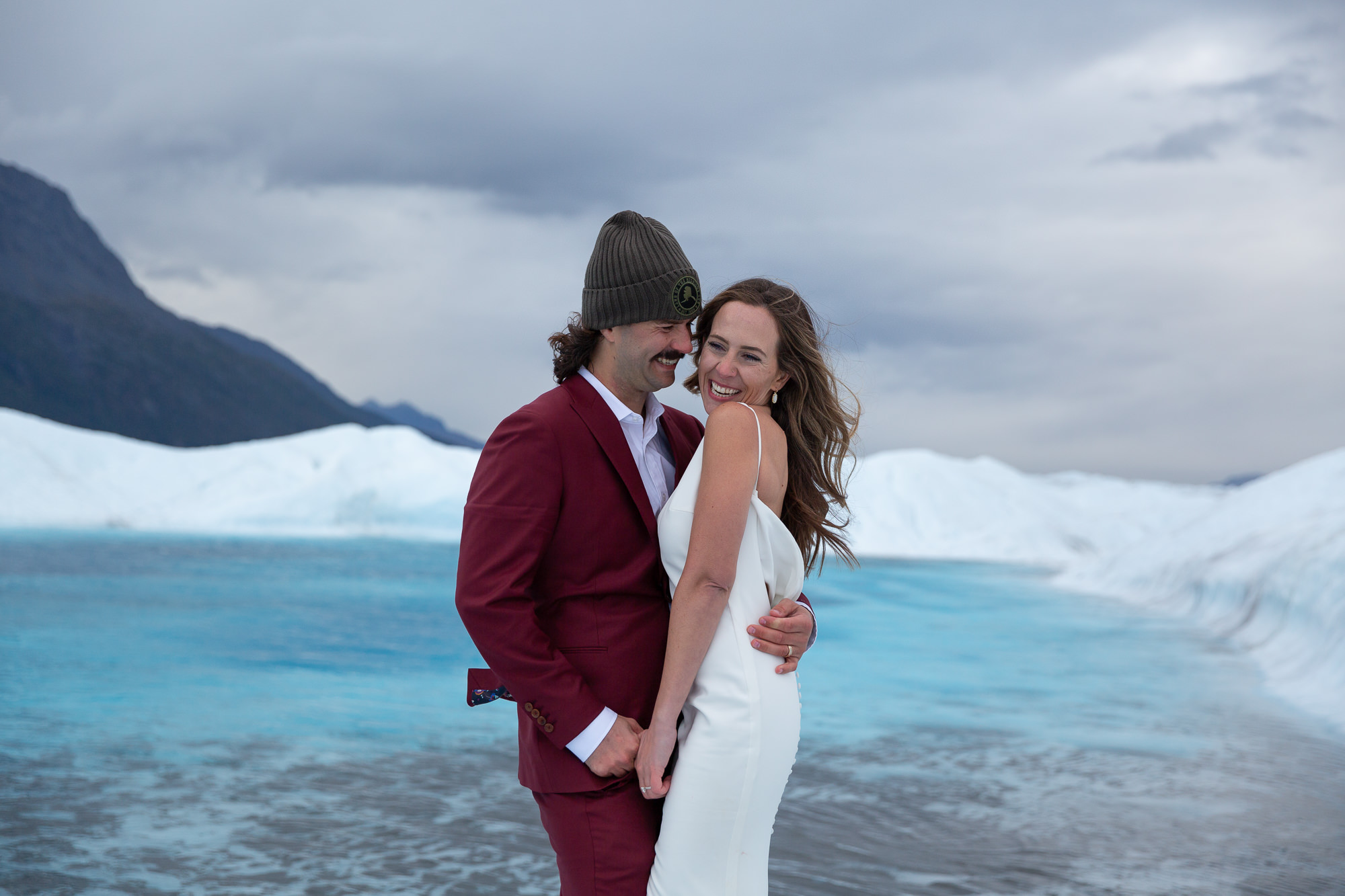 Couple embracing beside bright blue glacier ice at Knik Glacier, Alaska during a scenic elopement.