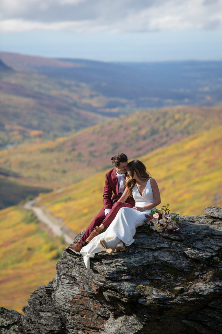 Bride and Groom sit side-by-side on a rock with rolling yellow hills behind them.