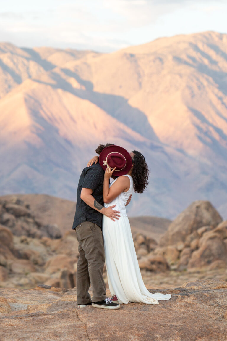 A bride and groom kiss behind a red hat on their alabama hills adventure elopement day.