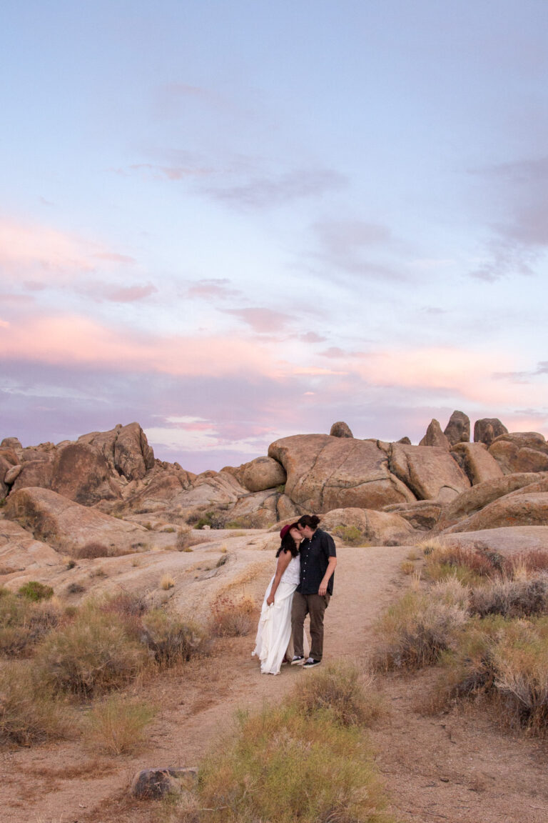 A bride and groom kiss as the walk along a dirt path in Alabama Hills on their elopement day.