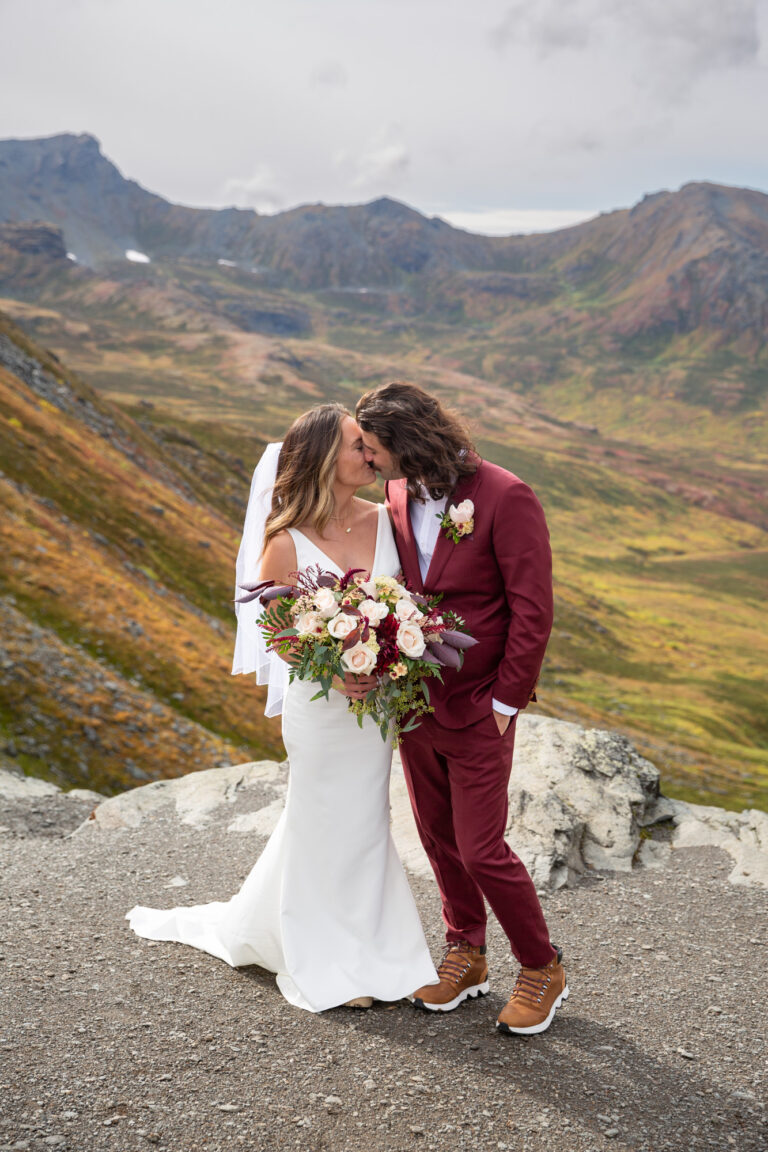 A bride and groom kiss on their Alaska elopement day while the bride holds a beautiful bouquet of flowers.