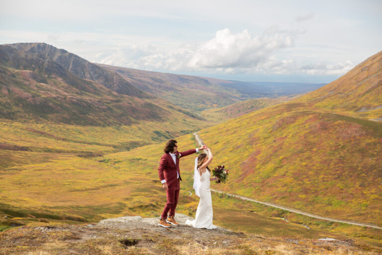 A groom twirls his bride as they stand on a rock at Hatcher Pass in Alaska.