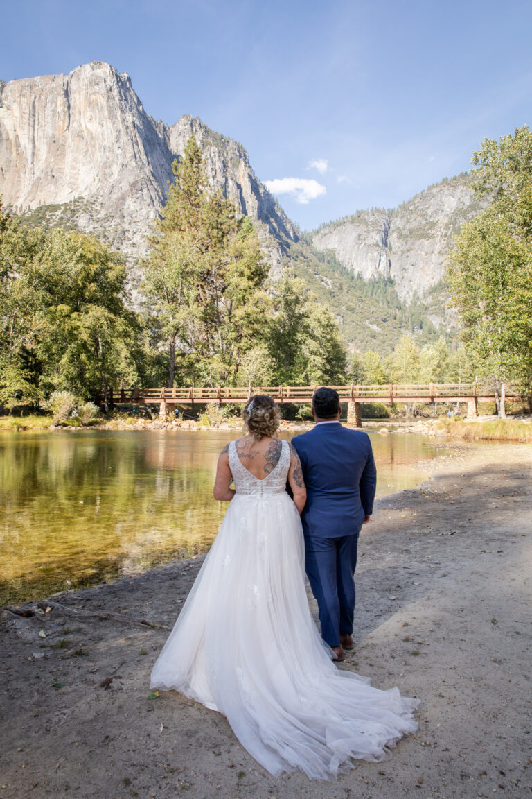 A bride and groom stand facing the mountains and the Merced River at after their elopement ceremony in Yosemite National Park.