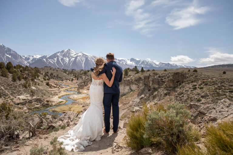 A bride and groom stand hugging each other as they look out at the Eastern Sierra Mountains in Mammoth on their elopement day - easily one of the best places in California to elope!