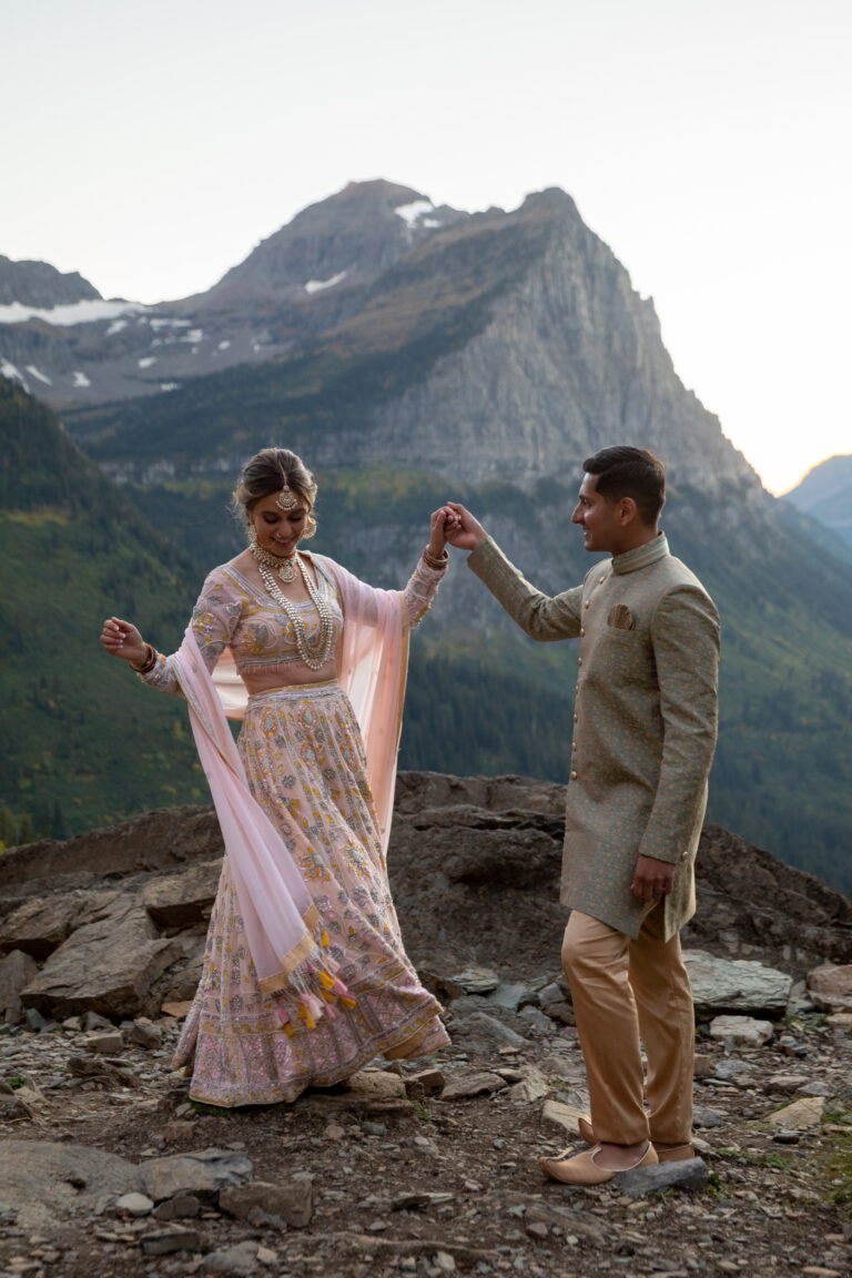 A bride and groom dressed in Indian wedding attire dance slowly together in Glacier National Park as the sunsets