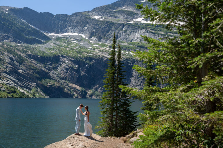A bride touches her groom's chest as they stand on a rock next to a lake in Montana on their wedding day.