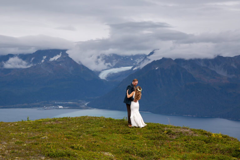 A bride and groom share their first dance on a grassy hill high above Resurrection Bay in Alaska