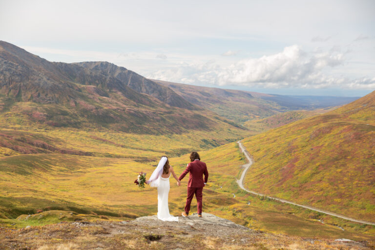 A bride and groom stand hand in hand at Hatcher Pass in Alaska on their wedding day.