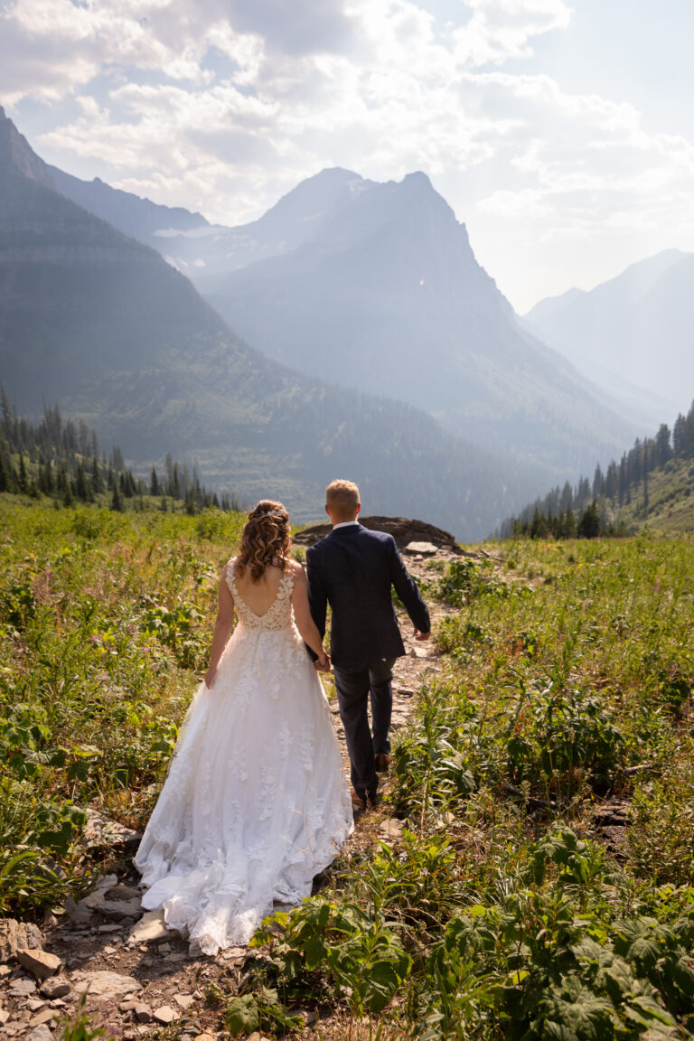 A bride and groom walk down a rocky path hand in hand