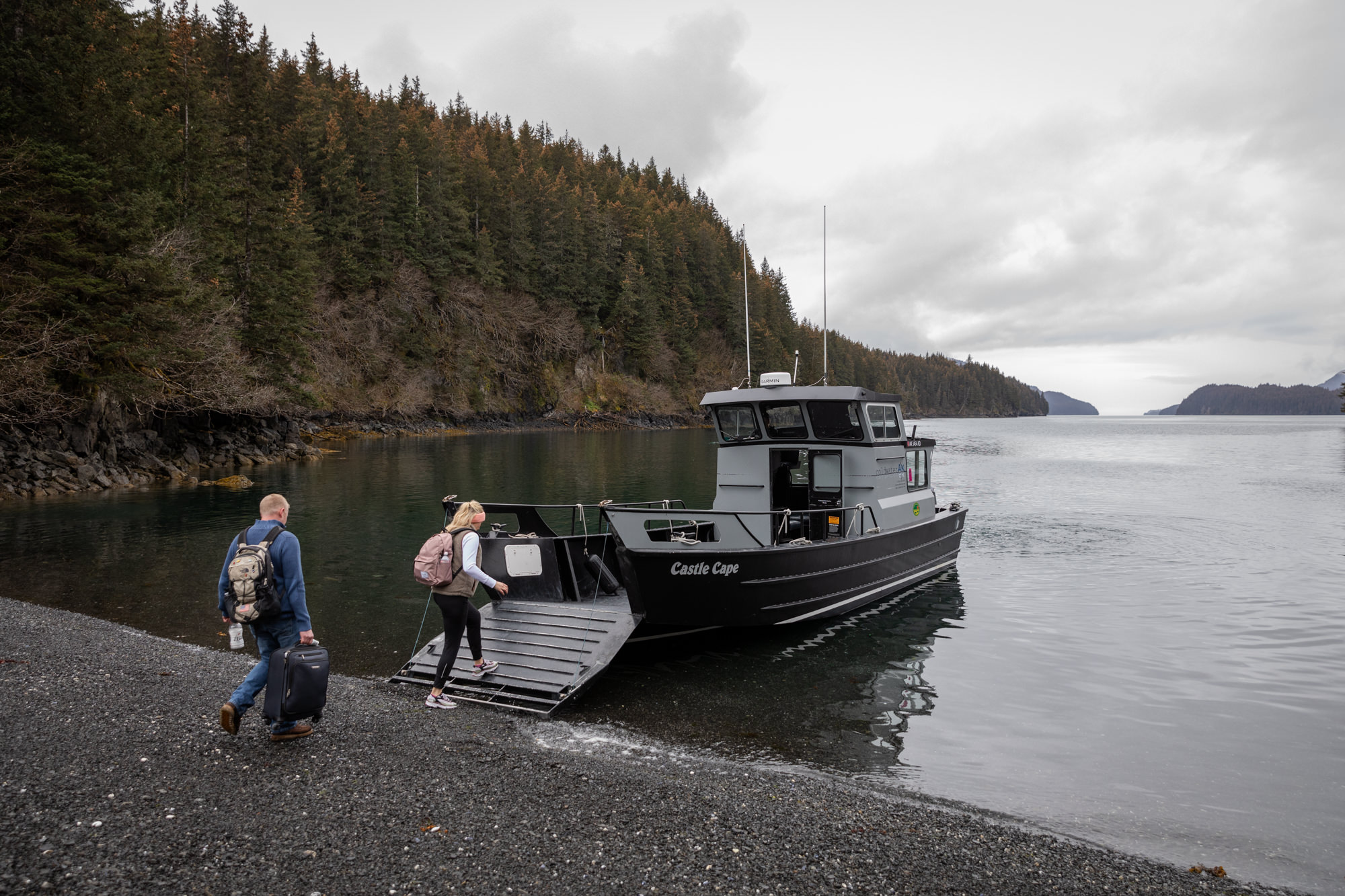 Couple boarding a small boat along a forested shoreline near Homer, Alaska during a coastal elopement adventure.