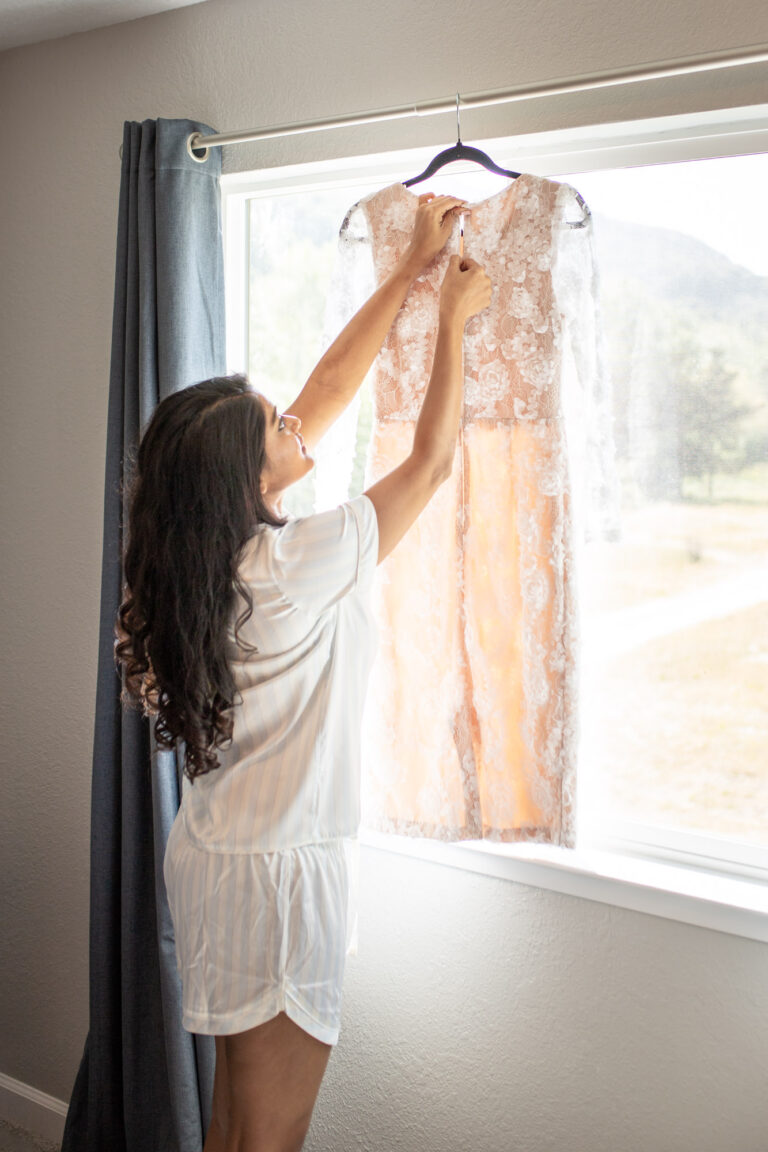 A bride unzips her wedding dress that is hanging in a window