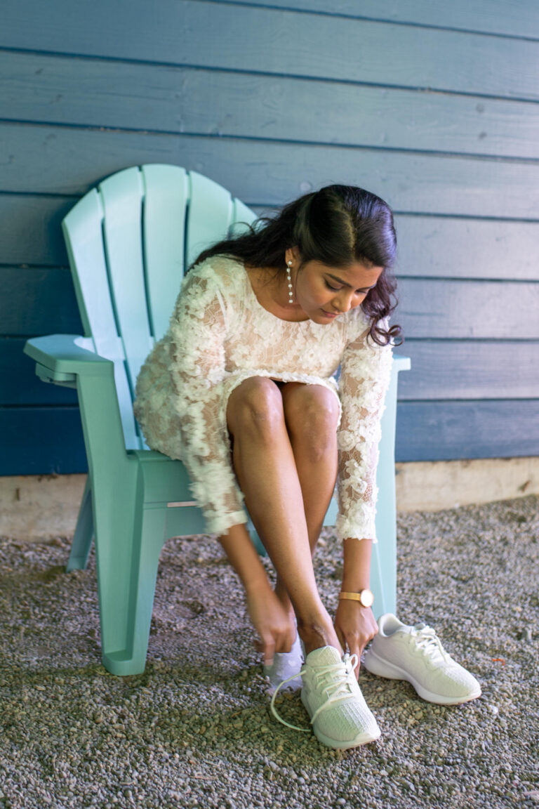 A bride puts her shoes on while sitting in a blue chair.