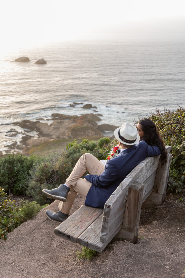 A bride and groom sit on a wooden bench in Big Sur after their ceremony.
