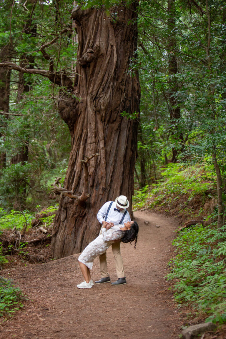 A groom dips his bride on a dirt path in the forest on their elopement day.