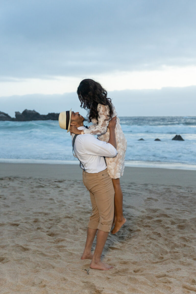 A groom lifts his bride up in the air on the beach in Big sur.