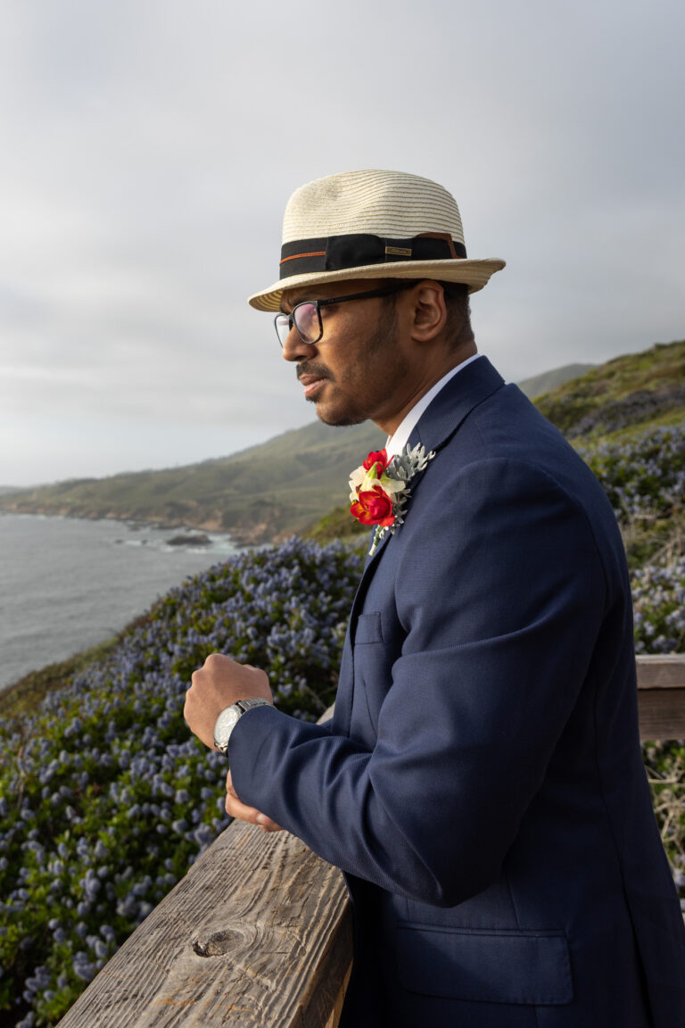 A groom stares out into the ocean as he adjusts his cufflinks