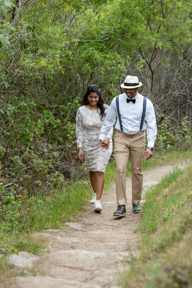 A bride and groom walk hand in hand along a dirt path on their cliffside wedding day.