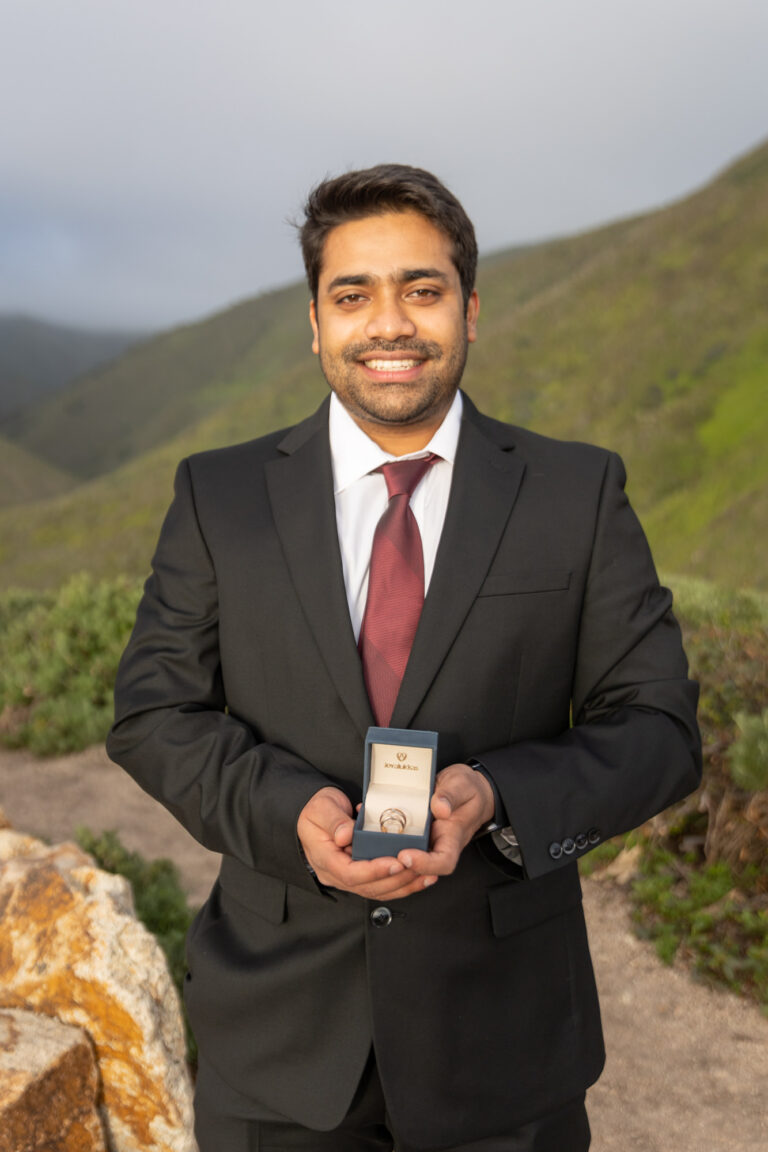 An officiant smiles at the camera as he holds the box with the wedding rings.