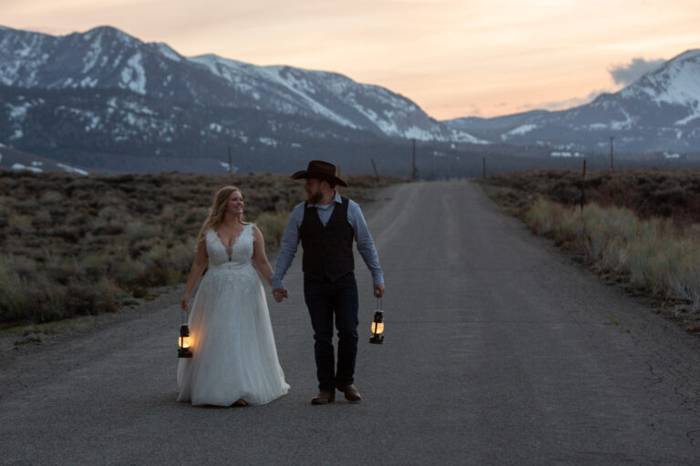 A bride and groom walk down a road as the sunsets behind them on their Convict Lake wedding day.