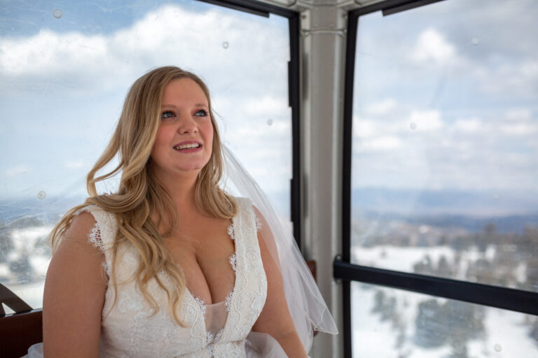 A bride sits in a gondola on her way up to the top of a mountain.