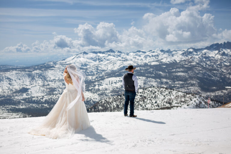 A bride stands facing her groom as he faces away from her while they stand on top of Mammoth Mountain.
