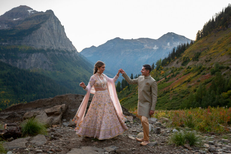 A bride and groom dance on some rocks with mountains behind them.
