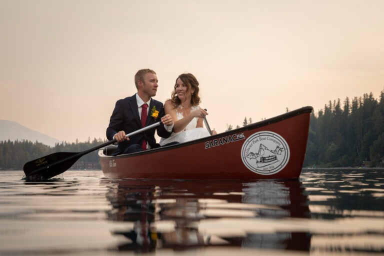 A couple sit side by side paddling a canoe on their elopement day in Glacier National Park