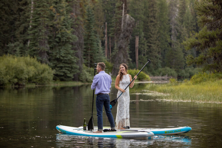 A bride and groom stand on paddle boards in the middle of a lake on their elopement day.