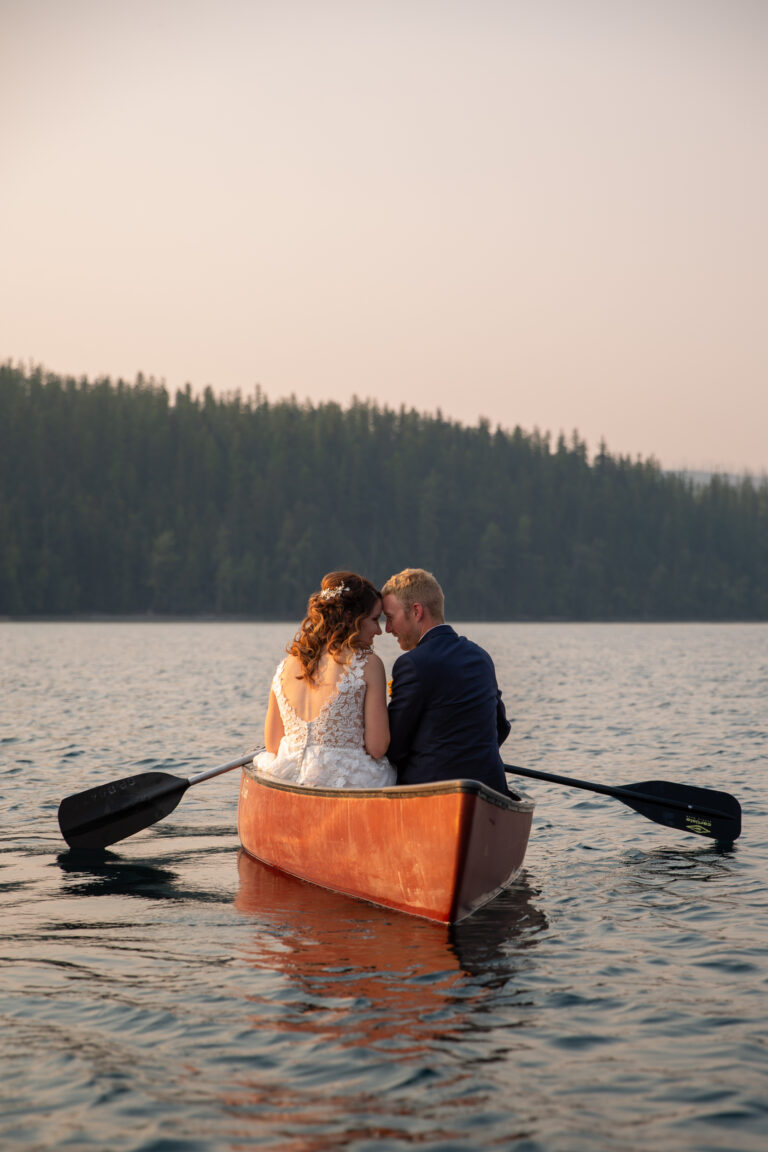 A couple sit side by side in a canoe on their elopement day in Glacier National Park with their foreheads touching.