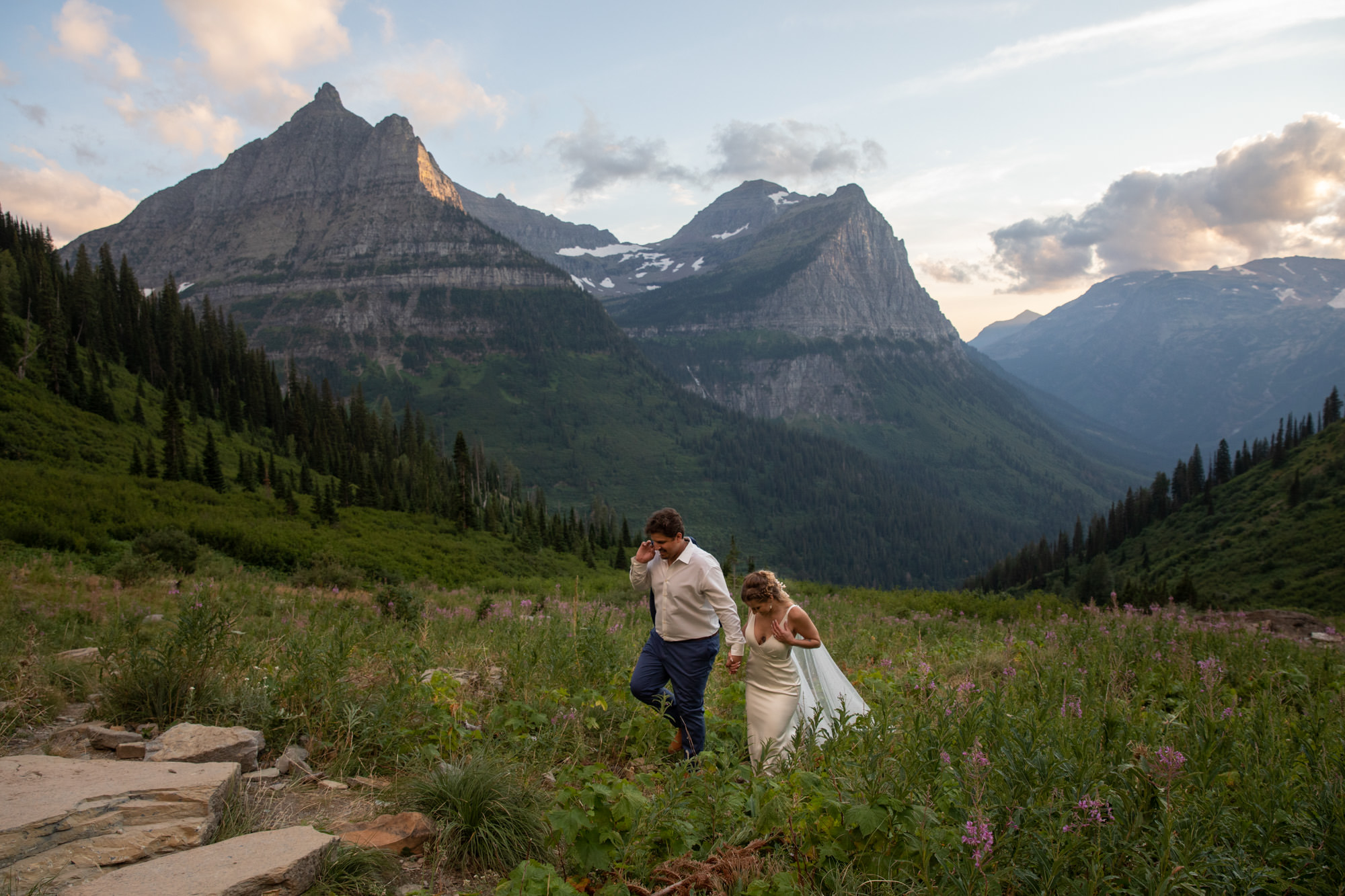 A bride and groom walk hand in hand along a trail after eloping in Glacier National Park.