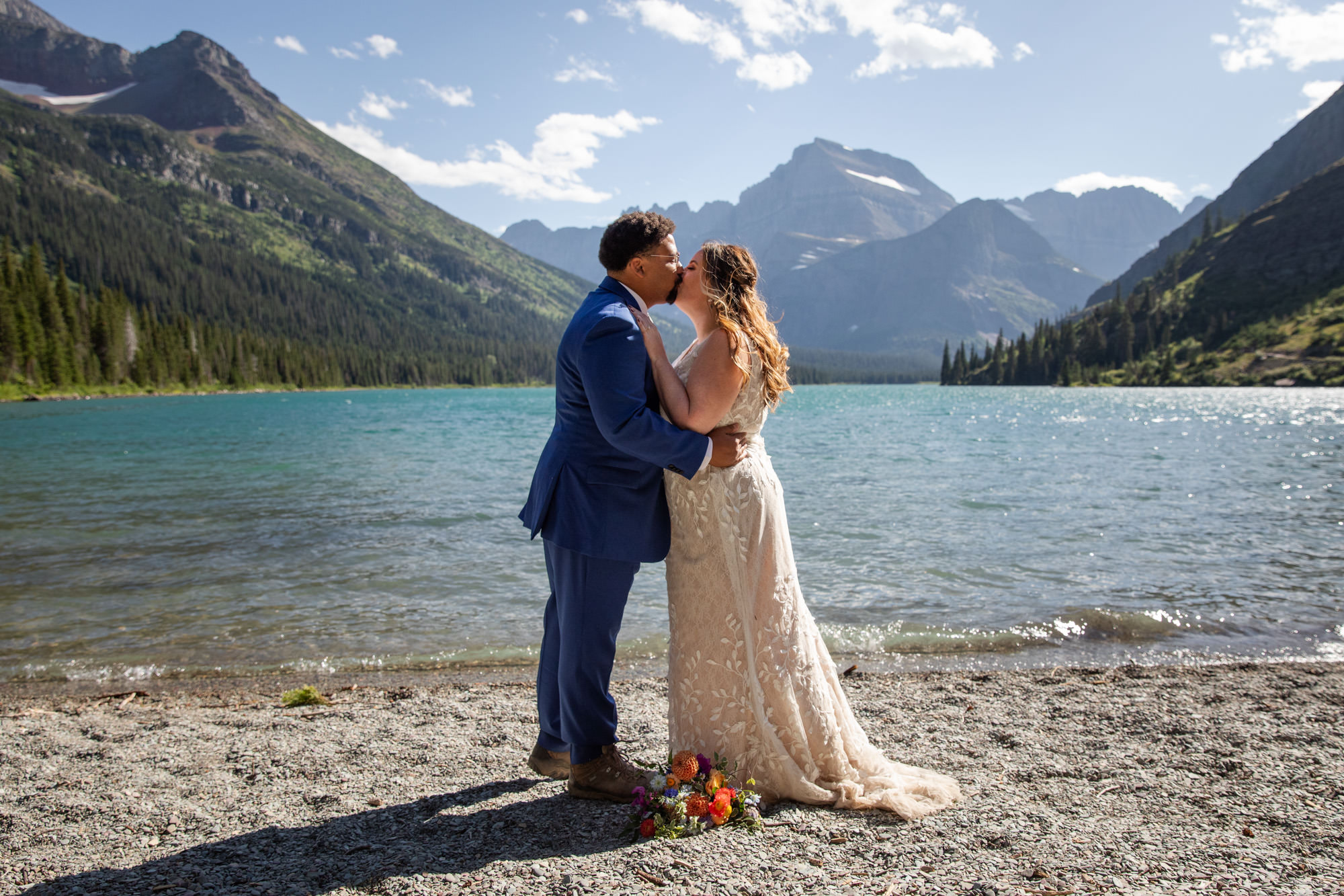 A bride and groom kiss on the shore of Lake Josephine after eloping in Glacier national park.