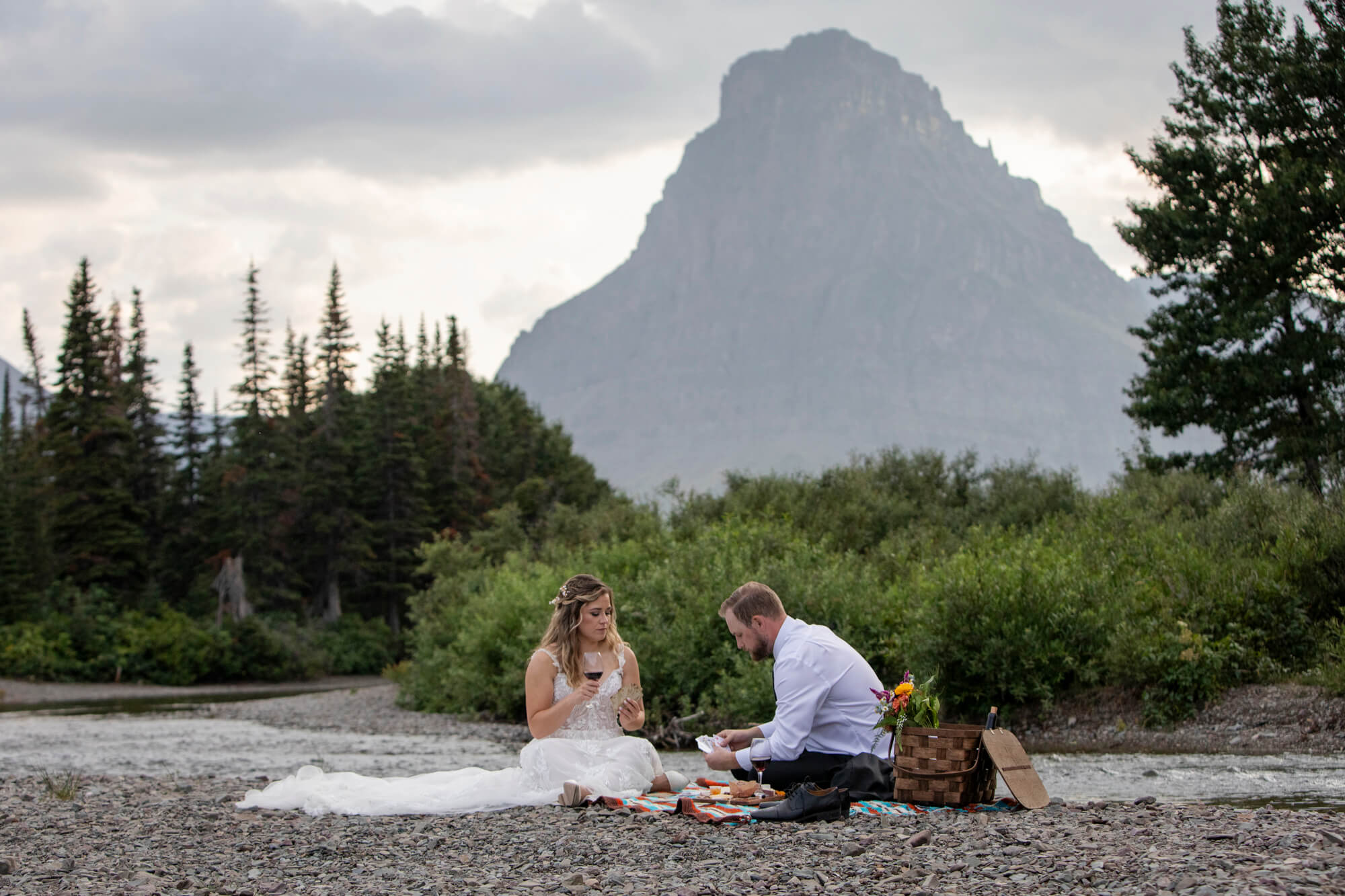 Eloping in Glacier National Park: Your Complete Guide | Scenic Vows A bride and groom sit on a blanket playing a card game on their elopement day in Glacier National Park.