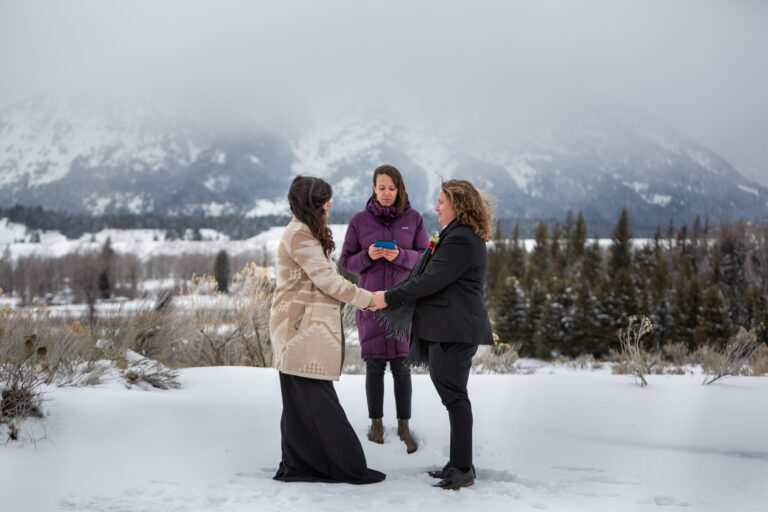 A couple stand face to face holding hands as the officiant reads the ceremony script at their elopement ceremony in Grand Teton National Park.