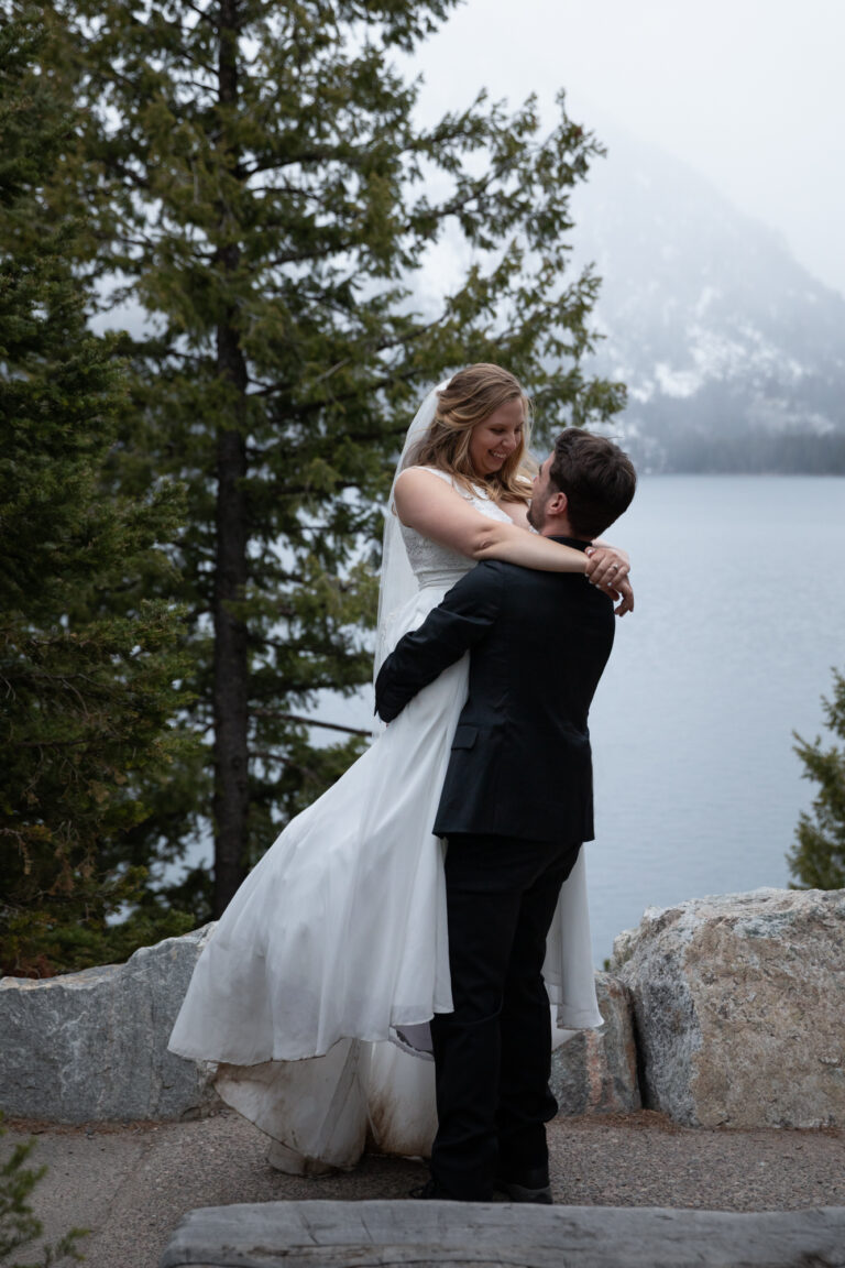 A groom lifts up his bride as she smiles down at him after eloping in Grand Teton.