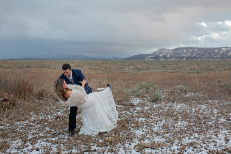 A groom dips his bride in a snow dusted field after eloping in Grand Teton.