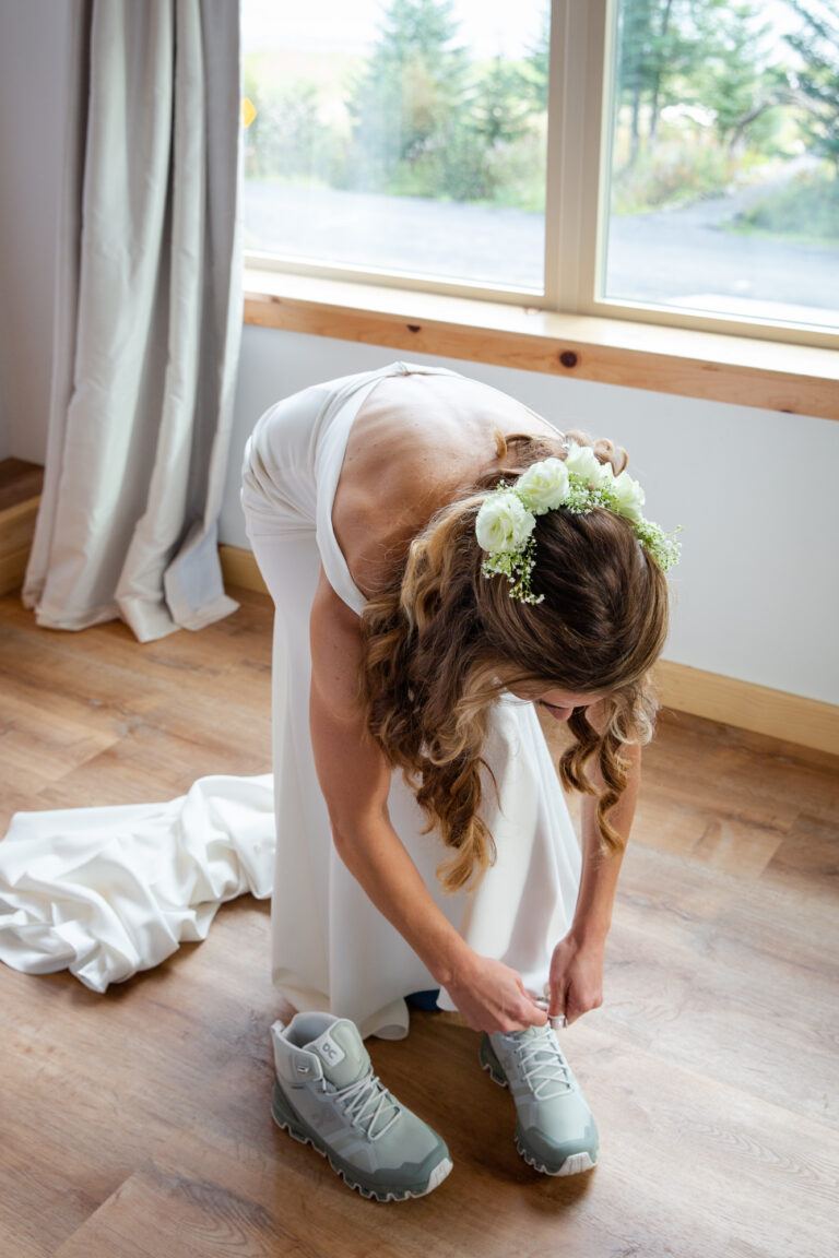 A bride bends over to tie her hiking boots on her helicopter elopement day.