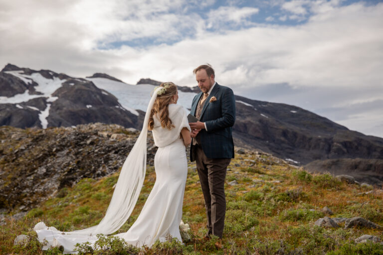 Groom reads his vows to his bride during their elopement ceremony surrounded by snow capped mountains in Alaska.
